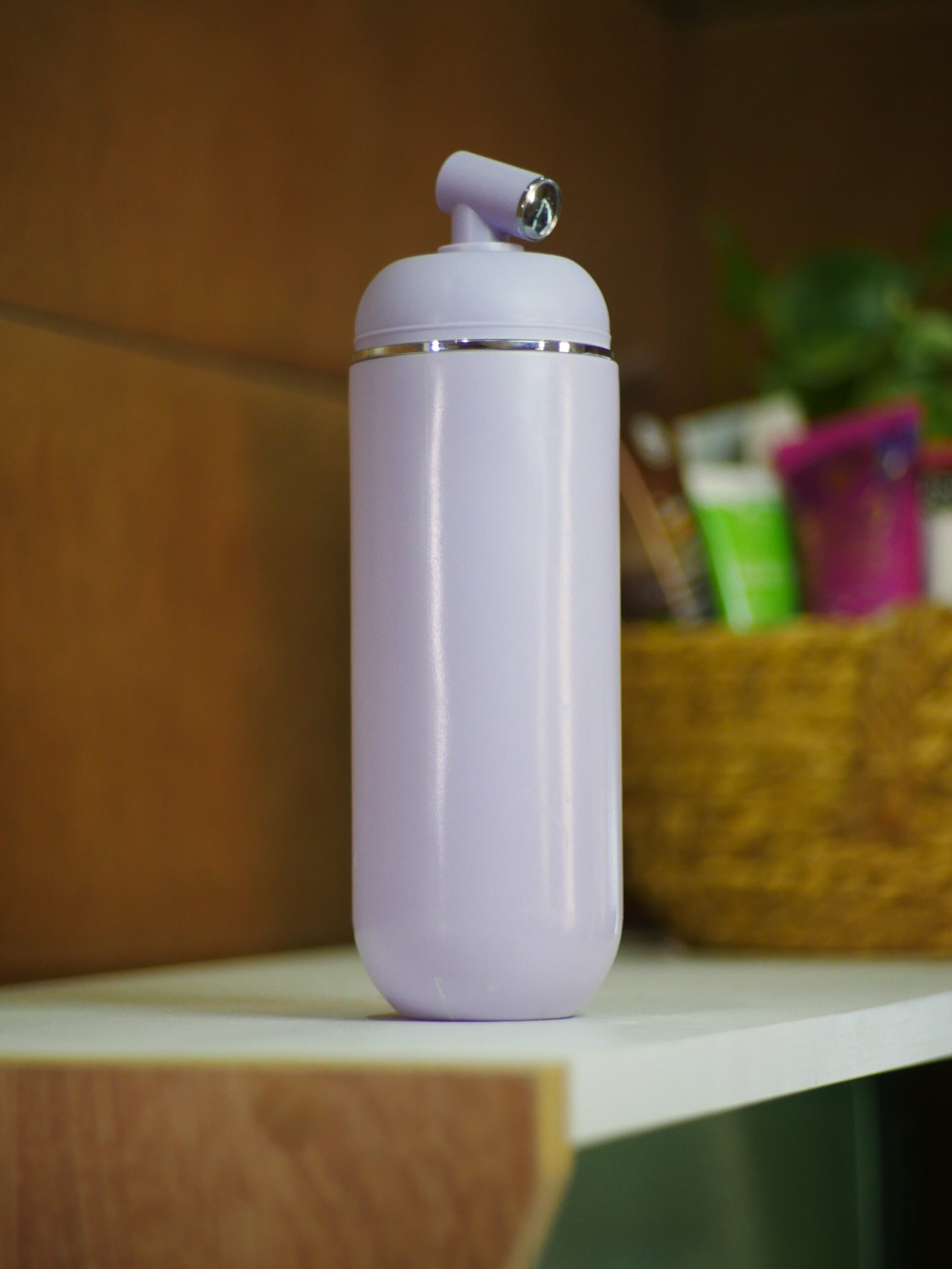 Portable water bidet in a sleek lavender design, featuring a nozzle and ergonomic shape, placed on a shelf.