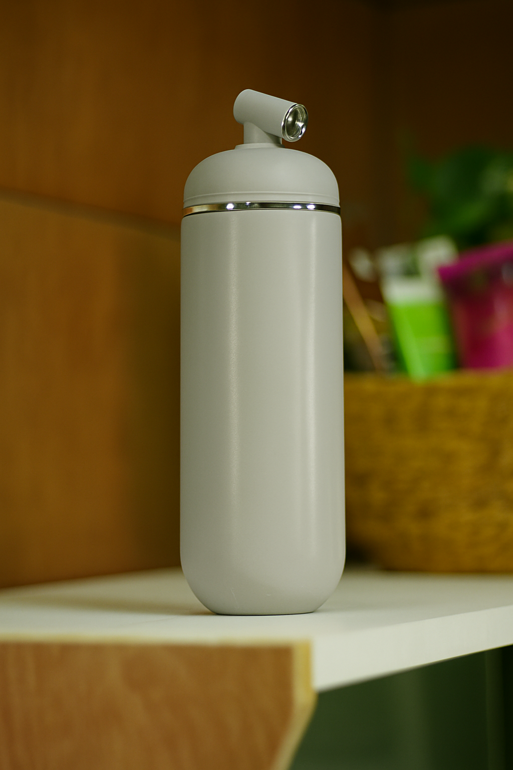 Portable cylindrical bidet bottle in a matte off-white light grey shade, displayed on a white shelf in a home setting.